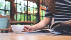 Woman reading a book with coffee at a table, concept scene for NGO coffee table book storytelling and social impact.