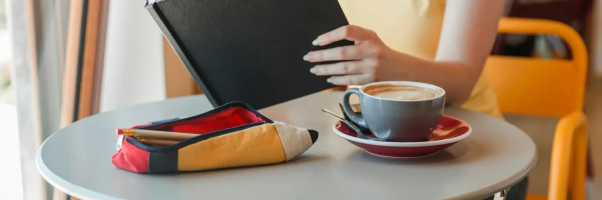 Person reading a coffee table book at a cafe table with coffee, representing impact storytelling visuals often used in annual reports.